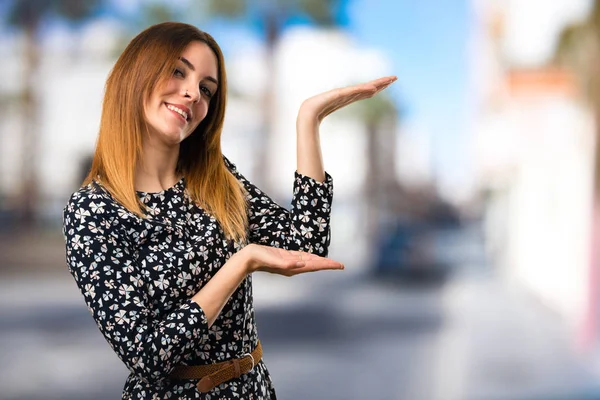 Schönes Junges Mädchen Das Etwas Auf Unkonzentriertem Hintergrund Präsentiert — Stockfoto