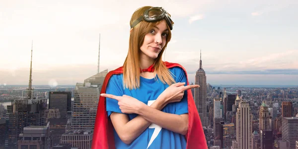 Pretty superhero girl pointing to the laterals having doubts in a skyscraper city