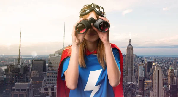 Pretty superhero girl with binoculars in a skyscraper city