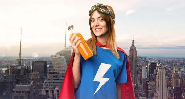 Pretty superhero girl holding a orange juice in a skyscraper city