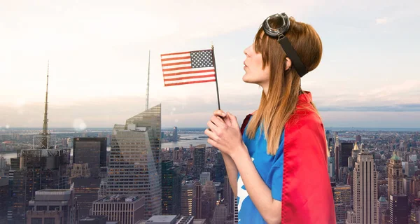 Pretty superhero girl holding an american flag in a skyscraper city