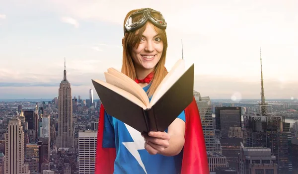 Pretty superhero girl reading book in a skyscraper city