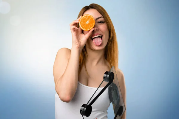 Beautiful young girl with weighing machine holding an orange on unfocused background