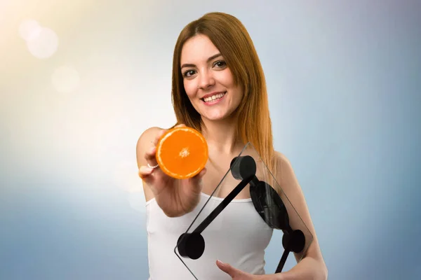 Hermosa Joven Con Máquina Pesaje Sosteniendo Una Naranja Sobre Fondo —  Fotos de Stock