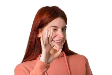 Pembe kazak izole beyaz arka plan üzerinde bir göz kırptı süre parmak ok işaretiyle gösterilen genç Kızıl saçlı kız