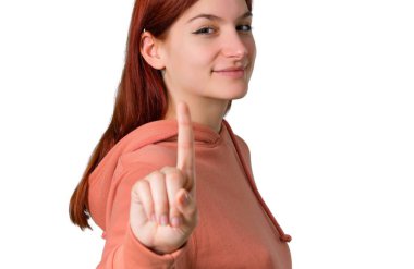 Genç Kızıl saçlı kız ile gösterilen ve işareti en iyi izole beyaz zemin üzerinde bir parmak kaldırma pembe kazak