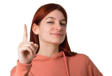 Genç Kızıl saçlı kız ile gösterilen ve işareti en iyi izole beyaz zemin üzerinde bir parmak kaldırma pembe kazak