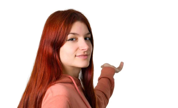 粉红色运动衫的年轻红头发的女孩指向后面的食指在独立的白色背景上呈现一个产品 — 图库照片