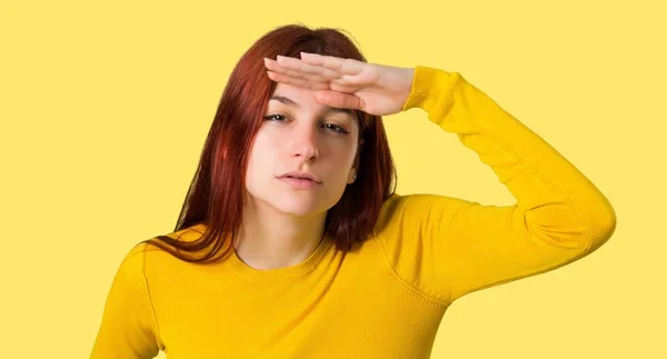 分離された黄色の背景で何かを見て黄色のセーター探して手で遠くの若い赤毛の女の子 — ストック写真