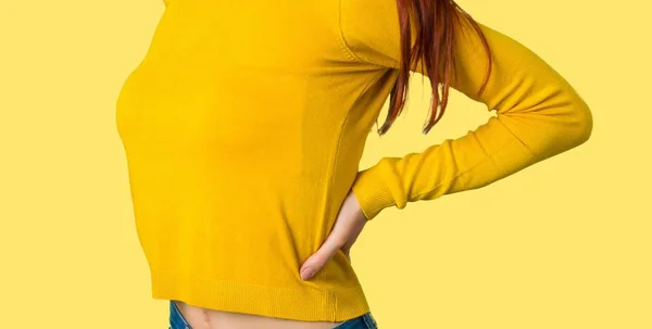 不幸と分離された黄色の背景に努力してきた腰痛に苦しんで黄色いセーターを着て 若い赤毛の女の子 — ストック写真