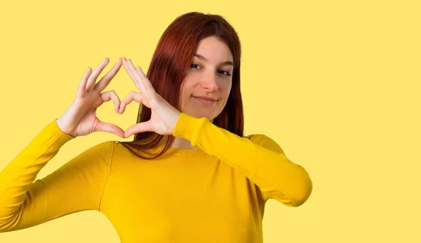 Chica Pelirroja Joven Con Suéter Amarillo Haciendo Símbolo Del Corazón —  Fotos de Stock