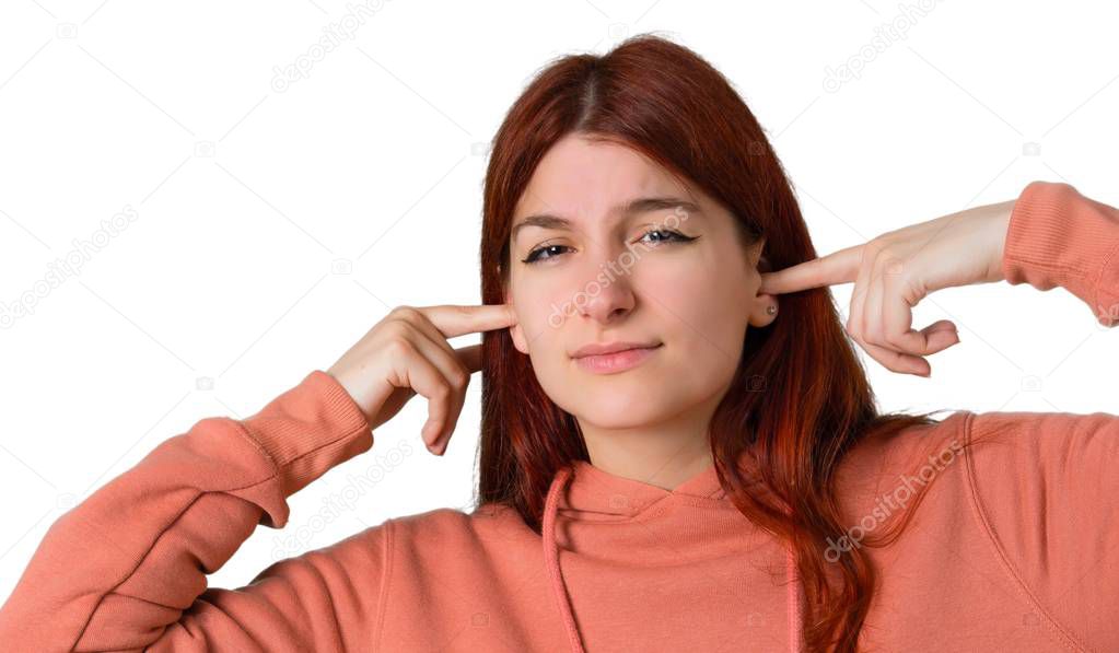 Young redhead girl with pink sweatshirt covering both ears with hands. Frustrated expression on isolated white background