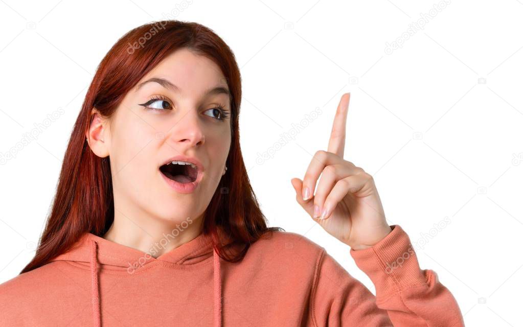 Young redhead girl with pink sweatshirt intending to realizes the solution while lifting a finger up on isolated white background