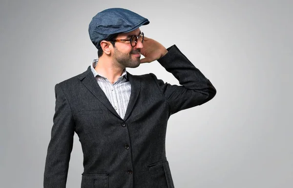 ベレー帽とメガネのグレーの背景上で何かを聞いて ハンサムな現代人 — ストック写真