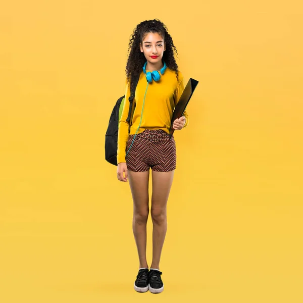 全身体的青少年学生女孩与卷曲的头发保持双臂交叉的正面位置 对黄色背景的自信表达 — 图库照片