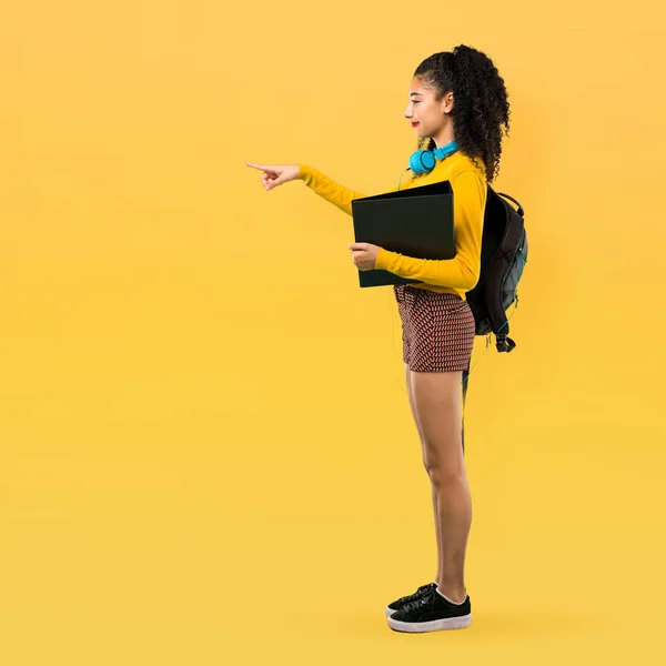 毛側に指を指すと 黄色の背景の横の位置に製品を提示 代学生の女の子の完全なボディ — ストック写真