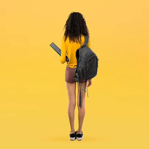 黄色の背景を振り返って巻き毛を持つ 代学生の女の子の完全なボディ — ストック写真