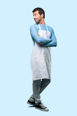 Mavi arka plan bir gülümseme ile omuz üzerinden bakarken yatay konumda bir önlük giyen adamın tam vücut