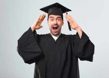 Sürpriz ve şok yüz ifadesi ile onun mezuniyet günü üniversite adamı. Çünkü ağzı açık gri arka plan üzerinde neler olduğunu inanamıyorum.