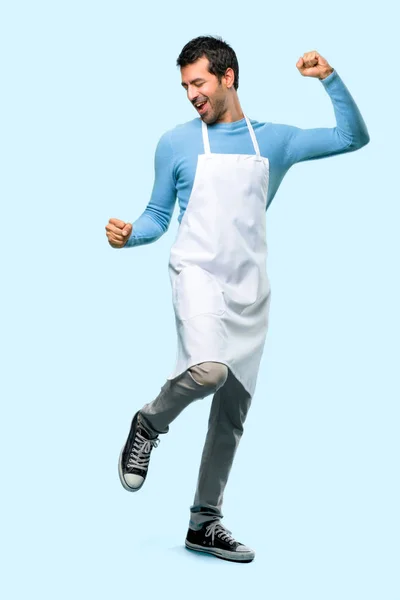 Full body of Man wearing an apron enjoy dancing while listening to music at a party on blue background