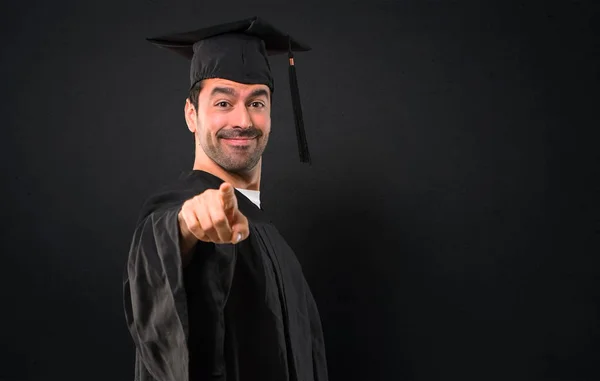 彼の卒業の日の大学の男が黒い背景に自信を持って式にあなたに指をポイントします — ストック写真
