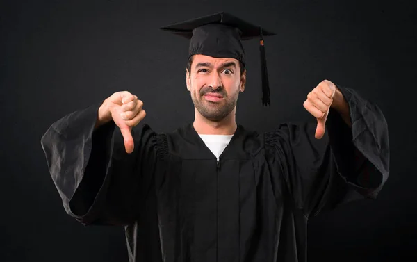 両方の手で親指を示す彼の卒業日大学の男 黒い背景に否定表現 — ストック写真