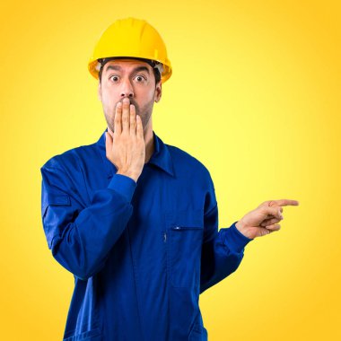 Parmak tarafına işaret ve sarı zemin üzerine ağız kapsayan süre sürpriz bir yüzle bir ürün sunma kask ile genç işçi