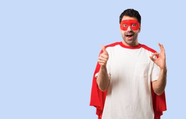Parmaklar ok işaretiyle gösterilen ve izole mavi arka plan üzerinde jest diğer elinizle bir başparmak veren maske ve kırmızı pelerin adamla süper kahraman