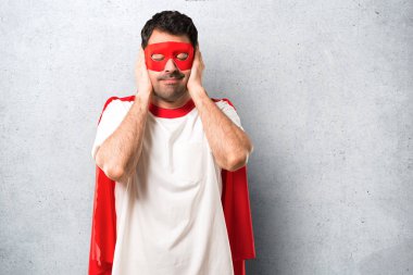 Süper kahraman maske ve kırmızı pelerin her iki kulak elleriyle kapsayan adamla. Dokulu gri arka plan üzerinde hayal kırıklığı ifade
