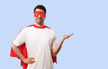 İzole mavi zemin üzerine bir reklam eklemek için maske ve kırmızı pelerin boşaltmak hayali avuç içinde tutan adamla süper kahraman