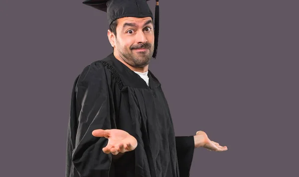 彼の卒業の日大学作り重要と紫色の背景で 肩と両手の手のひらを持ち上げながら疑問ジェスチャの男 — ストック写真