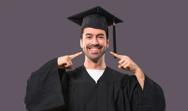 笑みを浮かべて彼卒業日大学紫色の背景に口と指で顔を指差しながら幸せと楽しい式と人 — ストック写真