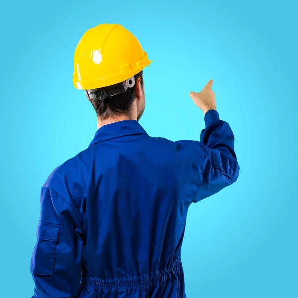 Young Workman Helmet Pointing Back Index Finger Blue Background — Stock Photo, Image