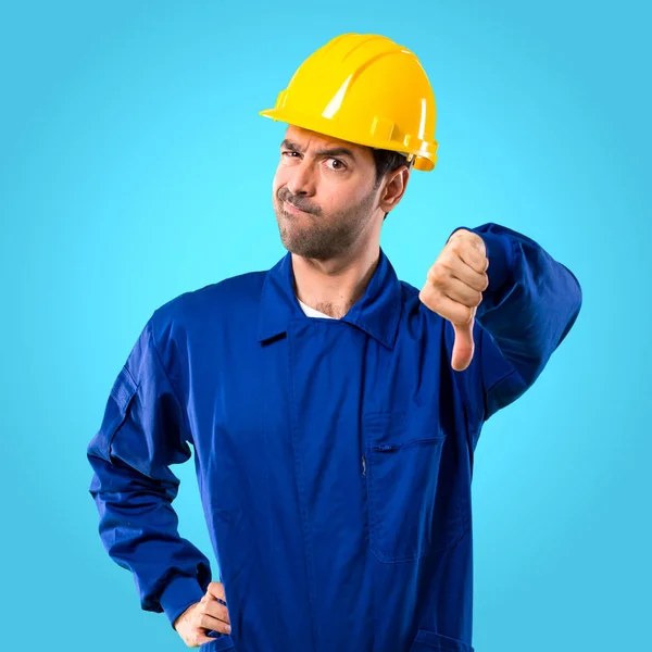 青の背景に親指で下を負の式と記号を示すヘルメットと若い職人 — ストック写真