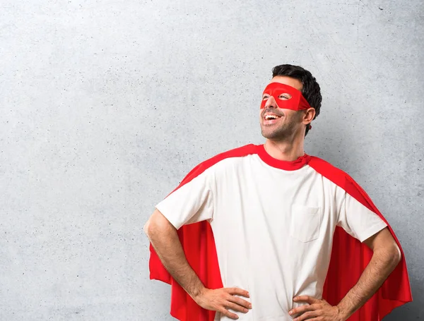 スーパー ヒーロー マスクと赤マントは ヒップで腕でポーズして 笑い質感の灰色の背景の人 — ストック写真