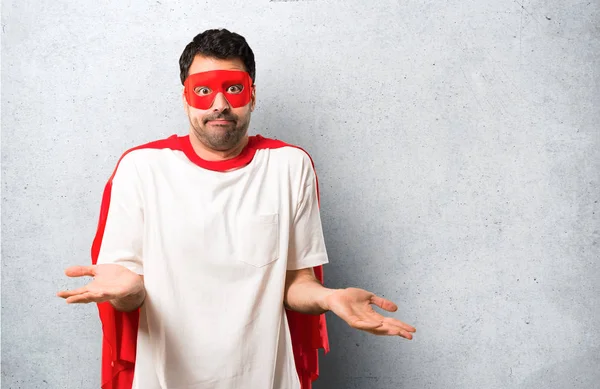 Superhero man with mask and red cape unhappy and frustrated with something because not understand something. Negative facial expression on textured grey background
