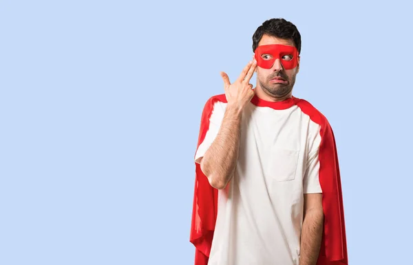 Superhero man with mask and red cape with problems and with unhappy expression making suicide gesture on isolated blue background