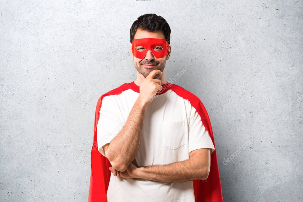 Superhero man with mask and red cape smiling and looking to the front with confident face on textured grey background