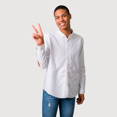 Gülümseyen ve neşeli bir yüz zafer işaretiyle gri arka plan üzerinde gösterilen genç Afro-Amerikan adam