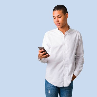 Beyaz gömlek izole mavi arka plan üzerinde bir ileti veya mobil ile e-posta gönderme ile genç Afro-Amerikan adam