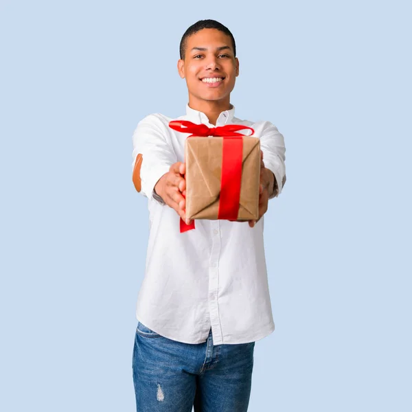 年轻的非洲裔美国男子与白色衬衫手持礼品盒在独立的蓝色背景手 — 图库照片