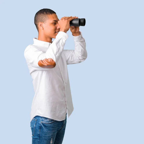 年轻的非洲裔美国人与白色衬衫和寻找东西在距离孤立的蓝色背景望远镜 — 图库照片