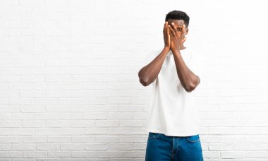 Gözleri eller tarafından kapsayan ve parmaklarının arasından seyir adam koyu tenli