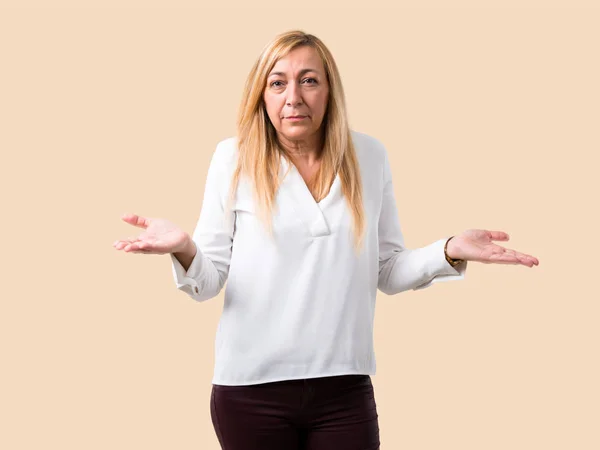 Middle age blonde woman with white shirt unhappy and frustrated with something because not understand something. Negative facial expression on isolated ocher background