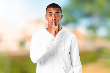 Esmer beyaz kazak ağız ve sessizlik kapanış bir işaret gösteren genç adamla jest bir parkta ağzına koyarak parmak