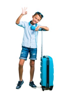 Çocuk tam vücut güneş gözlüğü ve kulaklık bavulunu bir ok işareti parmak ile izole beyaz arka plan üzerinde gösterilen ile seyahat ile