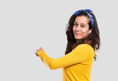 Sarı kazak ve geri bir ürün arkadan yalıtılmış gri arka plan üzerinde sunulması işaret parmağı ile işaret başında mavi bandana ile genç kız