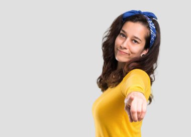 Sarı kazak ve parmağında baş noktaları size izole gri arka plan üzerinde kendine güvenen bir ifade ile mavi bandana ile genç kız