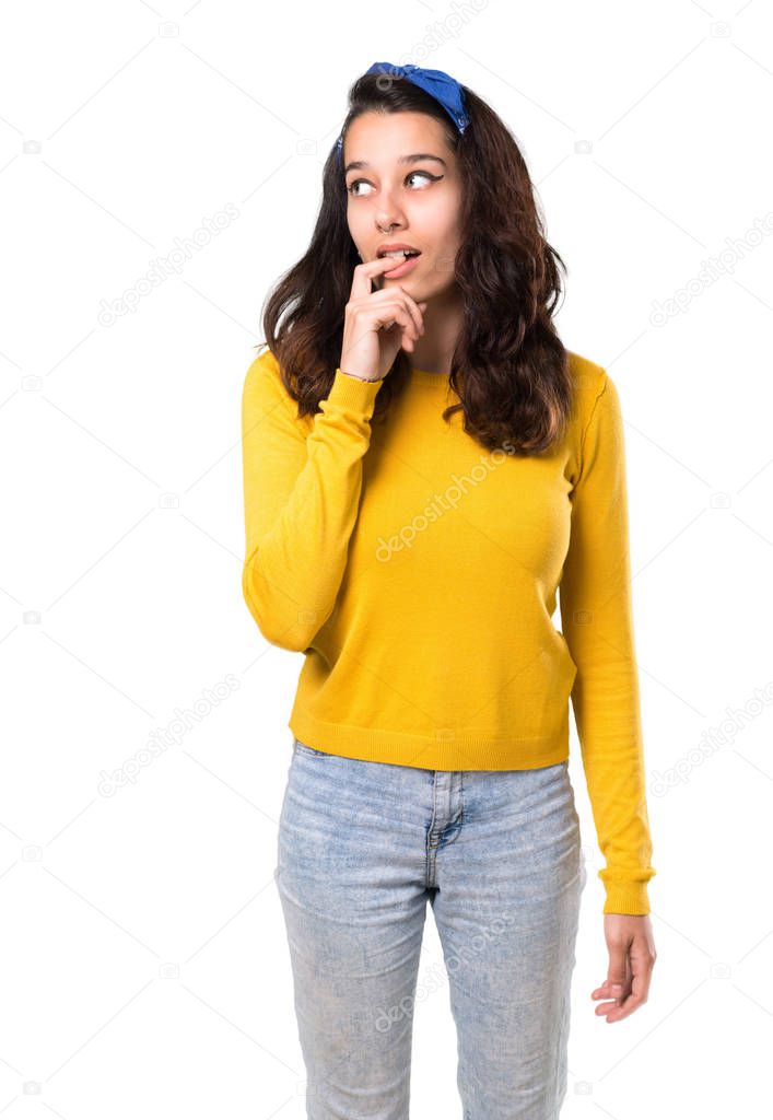 Young girl with yellow sweater and blue bandana on her head having doubts and with confuse face expression while looking up. Questioning an idea on isolated white background