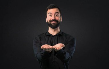 Bir şey siyah arka planda tutan sakallı yakışıklı adam